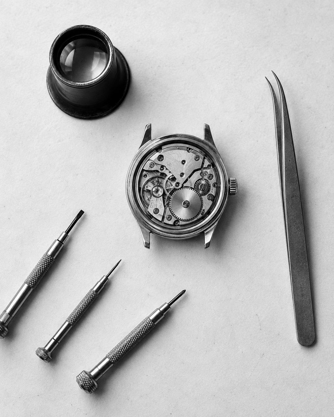 Loupe, tweezers, screwdrivers and an open case on a bench